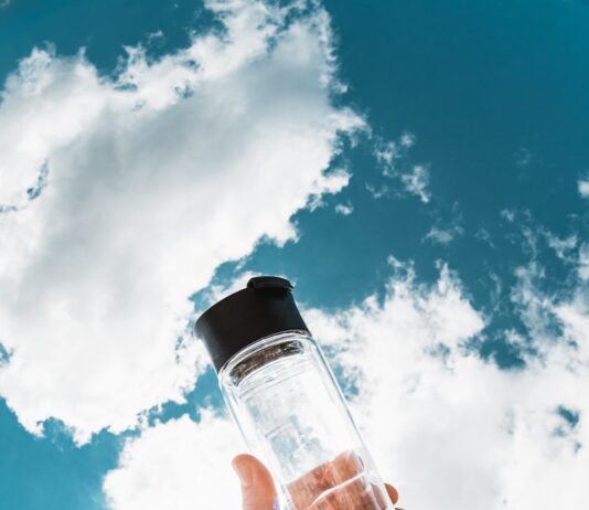 무더위 속 건강하게 여름 나기, 실천해야 할 생활 습관 a hand holding a water bottle in front of a blue sky