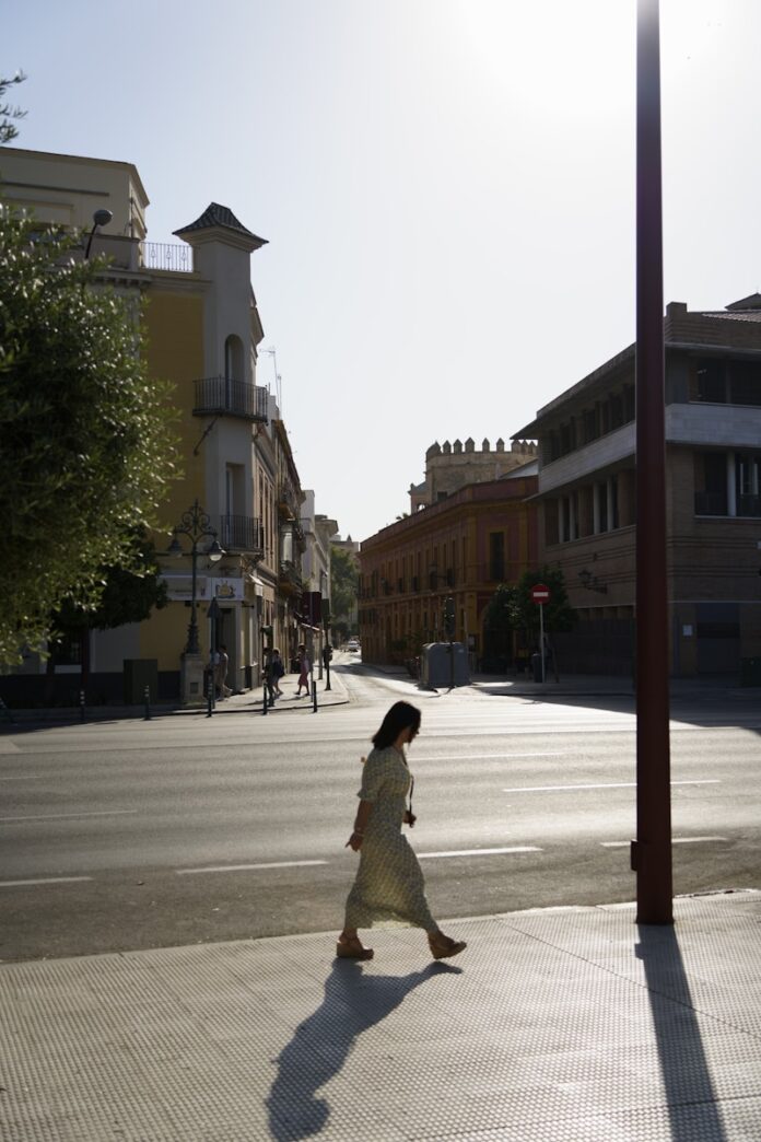 Photo by Hoyoun Lee A woman walking down a street next to tall buildings